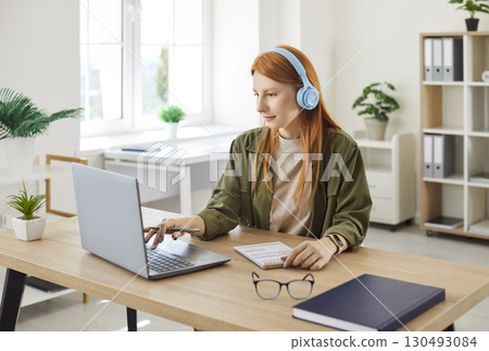 Young red hair girl, busy student wearing headphone watching laptop screen, listening online course Young red hair girl, busy student wearing headphone watching laptop screen, listening online course 130493084