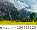 Majestic mountains rise in the background as quaint wooden cabins dot green landscape. A winding path guides a visitor through this serene Swiss alps. Grindelwald Jungfrau Bernese alps Switzerland. 130493123