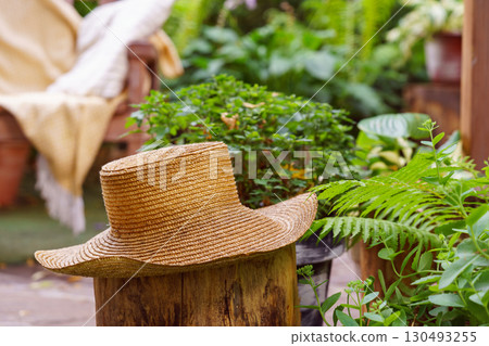 Rustic straw hat resting in lush garden with cozy armchair and soft throw in the background Rustic straw hat resting in lush garden with cozy armchair and soft throw in the background 130493255
