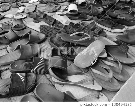 A chaotic jumble of various sandals and flip-flops, captured in a black and white image, scattered on a brick-paved ground. A chaotic jumble of various sandals and flip-flops, captured in a black and white image, scattered on a brick-paved ground. 130494185