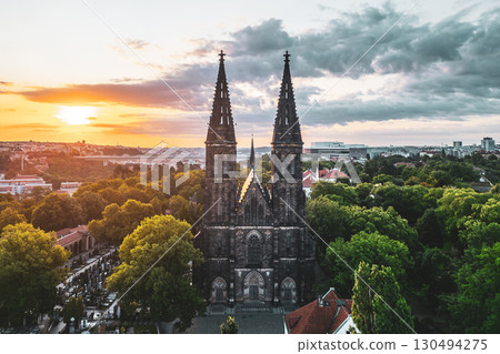 The morning light casts a warm glow on Vysehrad Basilica of St. Peter and St. Paul, illuminating its twin towers and surrounding greenery in the heart of Prague, Czechia. 130494275