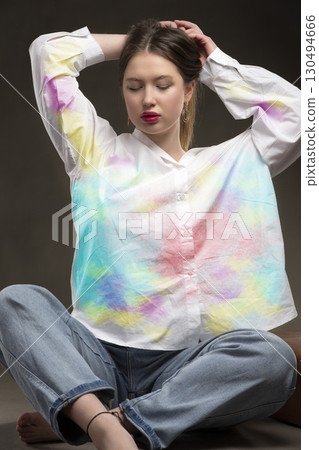A beautiful girl in a multi-colored shirt and jeans on a gray background. A beautiful girl in a multi-colored shirt and jeans on a gray background. 130494666