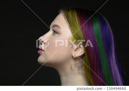 Profile of a young female model with perfect sensual lips and multi-colored strands of hair on a black background. Beautiful facial skin, augmentation of female lips, glamorous elegance. 130494668