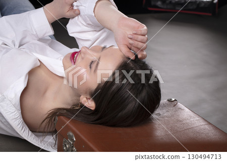 A beautiful girl lies on an old suitcase on a gray background. 130494713
