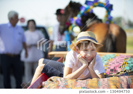 A funny little boy in a straw hat lies on a cart looking at the camera and smiles. A funny little boy in a straw hat lies on a cart looking at the camera and smiles. 130494750