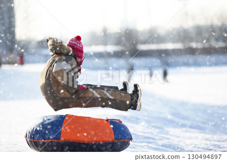 Little child on a sleigh. Child on a winter day. A boy is riding on a snow slide. 130494897