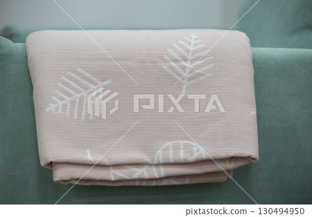 A pink coverlet with a floral motif rests on the green back of the sofa. A pink coverlet with a floral motif rests on the green back of the sofa. 130494950