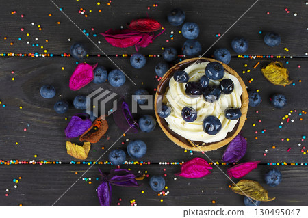 On a wooden board lies a cake with cream and blueberries. On a wooden board lies a cake with cream and blueberries. 130495047