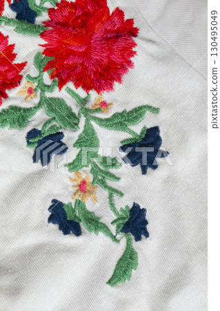 A piece of white cotton fabric with embroidered bright flowers. A piece of white cotton fabric with embroidered bright flowers. 130495049