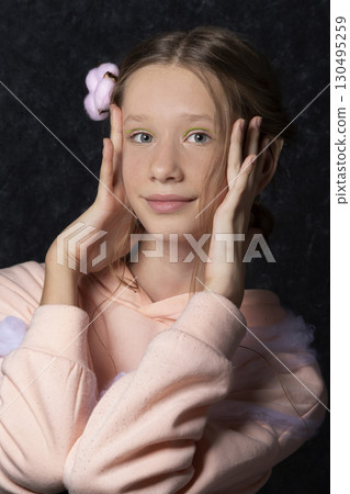 Portrait of a teenage girl in pink clothes on a dark background. 130495259