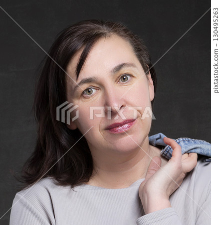 Beautiful fifty year old woman with dark hair on a gray background. Portrait of a middle-aged woman. Beautiful fifty year old woman with dark hair on a gray background. Portrait of a middle-aged woman. 130495263