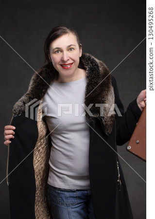 Happy fifty year old woman in a coat with a fur collar on a gray background. Portrait of a middle-aged woman. Happy fifty year old woman in a coat with a fur collar on a gray background. Portrait of a middle-aged woman. 130495268