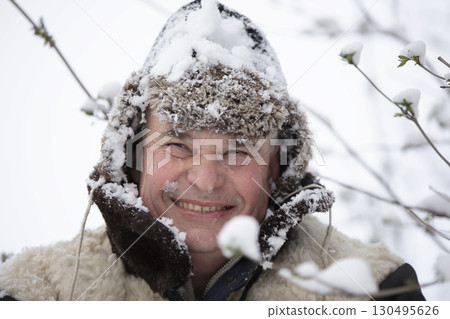 An elderly man in a winter hat covered with snow smiles and looks into the camera. 130495626