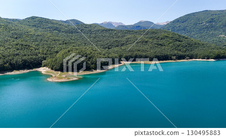 Serene turquoise lake surrounded by lush green mountains in the heart of nature's beauty Serene turquoise lake surrounded by lush green mountains in the heart of nature's beauty 130495883