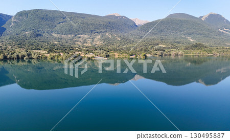 Calm waters reflect majestic mountains at a serene lake nestled in nature during a clear summer day 130495887