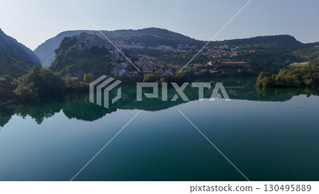 Serene reflection of a quaint village by a calm lake surrounded by mountains during a bright afternoon Serene reflection of a quaint village by a calm lake surrounded by mountains during a bright afternoon 130495889