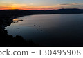 Sunset over tranquil waters reflecting vibrant colors near a serene harbor in a coastal village 130495908