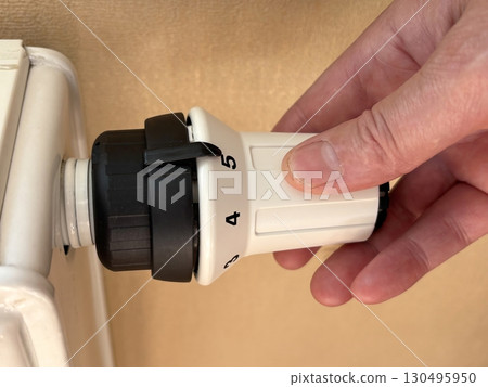 Woman hand unscrews radiator valve to supply heat. Cold weather, start of heating season, adjusting room temperature, home heating and comfort during winter concept Woman hand unscrews radiator valve to supply heat. Cold weather, start of heating season, adjusting room temperature, home heating and comfort during winter concept 130495950