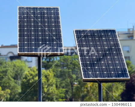 Two solar panels face the bright sky surrounded by green trees and buildings. Renewable energy, sustainability, and technology emphasize innovation, environment, and modern urban development. Two solar panels face the bright sky surrounded by green trees and buildings. Renewable energy, sustainability, and technology emphasize innovation, environment, and modern urban development. 130496011