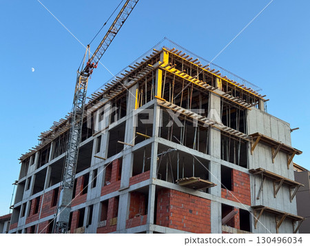 Concrete building under construction with crane and visible framework. Architecture, engineering, and urban development process in progress within a modern residential project. 130496034