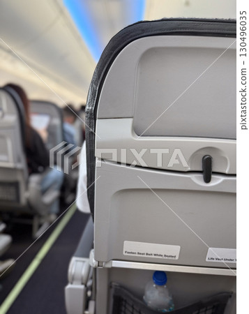 Aircraft cabin interior with passenger seat back and safety instructions. Aviation, travel, and passenger service equipment for flight safety and onboard comfort system. 130496035