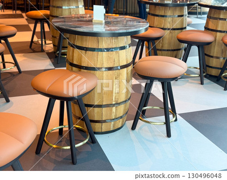 Cafe table made from wooden barrel with round cushioned stools around it. Illustration of decor, leisure, and travel lifestyle through dining, hospitality, and social gathering. 130496048