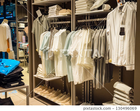 Menswear shop with folded shirts and clothing racks. Retail, fashion and consumer lifestyle in shopping environment. Menswear shop with folded shirts and clothing racks. Retail, fashion and consumer lifestyle in shopping environment. 130496069