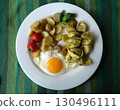 A vegetarian dish with pesto tortellini, a fried egg, new potato salad, cherry tomatoes, and a basil sprig. 130496111