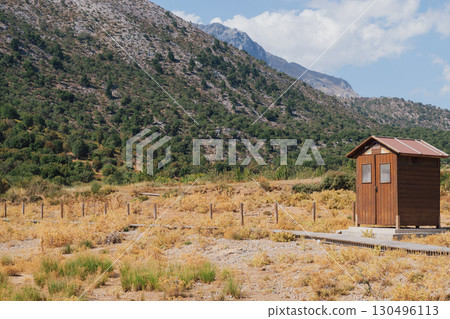 Wooden brown outdoor toilet cabin at the foot of mountains on sunny summer day Wooden brown outdoor toilet cabin at the foot of mountains on sunny summer day 130496113