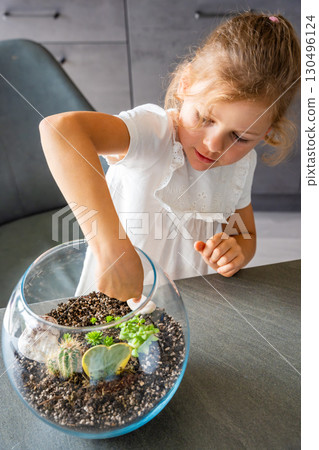 Little girl arranging soil, planting cacti and decorating a terrarium with stones and shells. Concept of creativity, eco-conscious learning and hands-on nature-based activity in childhood Little girl arranging soil, planting cacti and decorating a terrarium with stones and shells. Concept of creativity, eco-conscious learning and hands-on nature-based activity in childhood 130496124