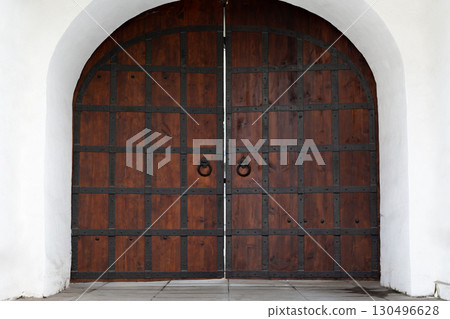 Old wooden gates with metal reinforcements and large ring handles, designed in a medieval or gothic style. Symbolizing strength, protection, and timeless craftsmanship 130496628