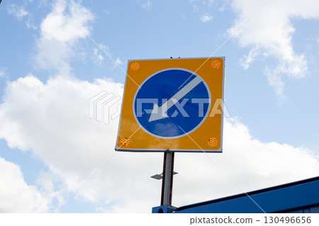 Road sign with blue circle and downward arrow, enhanced by glowing orange dots at each corner for increased visibility, ensuring safe and clear traffic direction even in low light conditions Road sign with blue circle and downward arrow, enhanced by glowing orange dots at each corner for increased visibility, ensuring safe and clear traffic direction even in low light conditions 130496656
