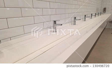 Modern public restroom with white tiled walls and chrome faucets Modern public restroom with white tiled walls and chrome faucets 130496720