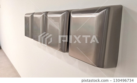 Row of stainless steel hand dryers on white tiled wall in public restroom Row of stainless steel hand dryers on white tiled wall in public restroom 130496734