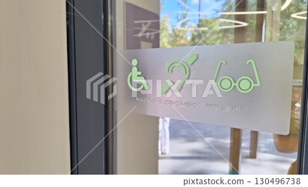Accessible entrance with disability symbols on glass door in sunlit building Accessible entrance with disability symbols on glass door in sunlit building 130496738