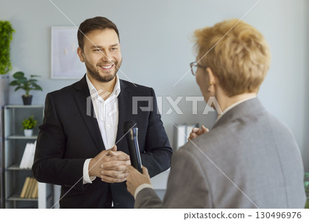 Woman journalist with a microphone interviewing attractive young man indoors 130496976