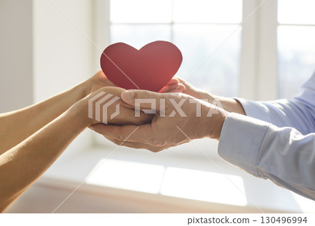 Two pairs of hands gently holding red paper heart together, showing love, support, care and romance. 130496994