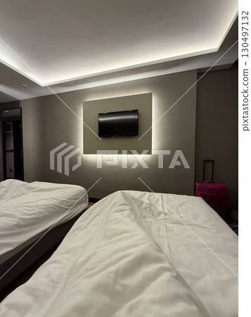 Hotel room interior with beds and illuminated wall-mounted television. Hospitality, travel, and lifestyle representing rest, comfort, and modern lodging atmosphere. 130497132