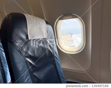 Airplane seat by window with visible wing under blue sky. Travel, aviation, and comfort representing passenger journey, mobility, and tourism lifestyle. Airplane seat by window with visible wing under blue sky. Travel, aviation, and comfort representing passenger journey, mobility, and tourism lifestyle. 130497189