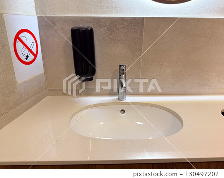 Bathroom sink with faucet, soap dispenser and no smoking sign on wall. Hygiene, facility, and modern design highlighting cleanliness, caution, and sanitary routine. Bathroom sink with faucet, soap dispenser and no smoking sign on wall. Hygiene, facility, and modern design highlighting cleanliness, caution, and sanitary routine. 130497202
