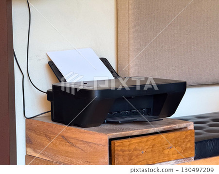 Printer placed on wooden cabinet with paper sheet ready for use. Technology, office equipment, and workplace productivity symbolizing function, utility, and communication. 130497209