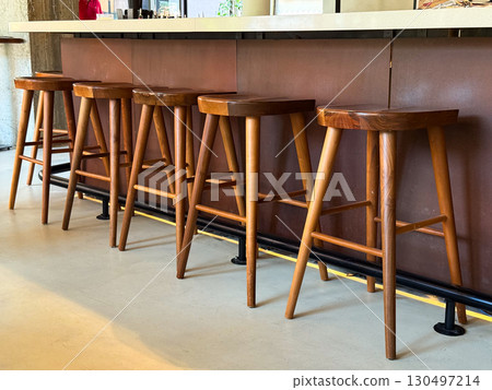 Wooden bar stools arranged neatly along counter in cozy interior. Seating, hospitality, and lifestyle atmosphere highlighting furniture design and social space furnishing. 130497214