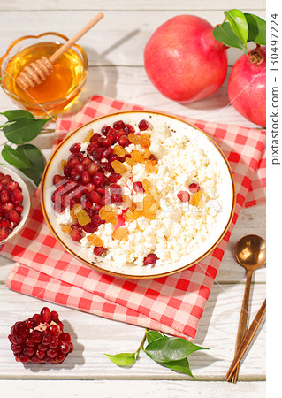 Granular fresh cottage cheese with pomegranate seeds, raisins, honey and juice on a sunny table, detox diet and natural nutrition concept, healthy lifestyle advertising, baby food. Healthy breakfast Granular fresh cottage cheese with pomegranate seeds, raisins, honey and juice on a sunny table, detox diet and natural nutrition concept, healthy lifestyle advertising, baby food. Healthy breakfast 130497224
