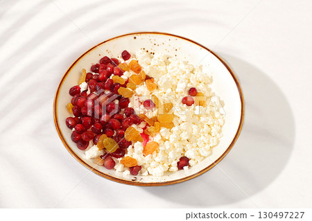 Granular fresh cottage cheese with pomegranate seeds and raisins on a sunny table, natural nutrition concept, healthy lifestyle advertising, baby food. Healthy breakfast with ingredients, menu for Granular fresh cottage cheese with pomegranate seeds and raisins on a sunny table, natural nutrition concept, healthy lifestyle advertising, baby food. Healthy breakfast with ingredients, menu for 130497227