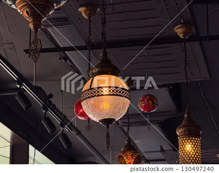 Hanging lanterns with colorful mosaic glass and brass frames glowing warmly. Traditional craft, cultural heritage, and artistic interior lighting creating atmosphere and hospitality. 130497240