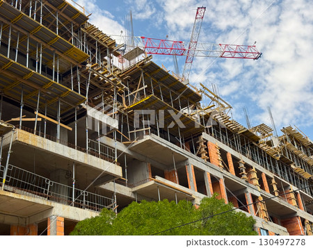 Brick walls and scaffolding at a construction site with a crane above. Architectural growth, structural engineering and urban expansion. Brick walls and scaffolding at a construction site with a crane above. Architectural growth, structural engineering and urban expansion. 130497278