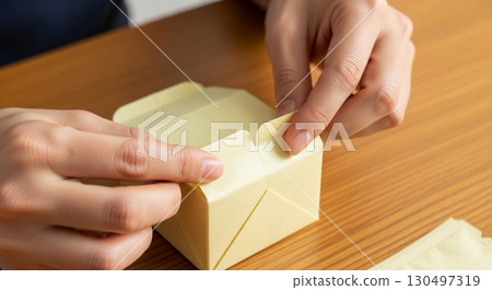 Hands of a diligent worker are folding lightweight, biodegradable packaging made from vegetable starch into a compact box, showcasing craftsmanship and sustainability. Hands of a diligent worker are folding lightweight, biodegradable packaging made from vegetable starch into a compact box, showcasing craftsmanship and sustainability. 130497319