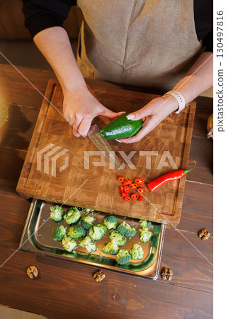 Woman slicing fresh avocado on wooden cutting board in cozy rustic kitchen 130497816
