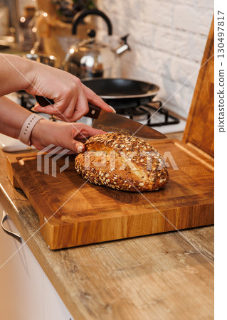 Slicing multigrain bread on a wooden board in a cozy home kitchen environment 130497817