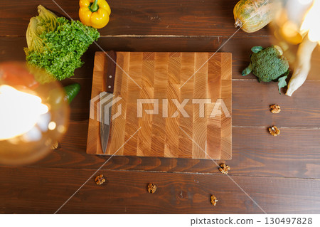 Top view of cutting board with knife surrounded by fresh vegetables on a rustic wooden table 130497828
